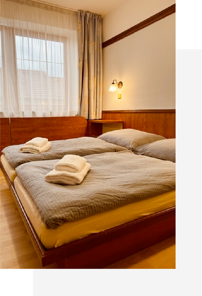 Hotel room with two single beds side by side, each with gray bedding and folded white towels on top.