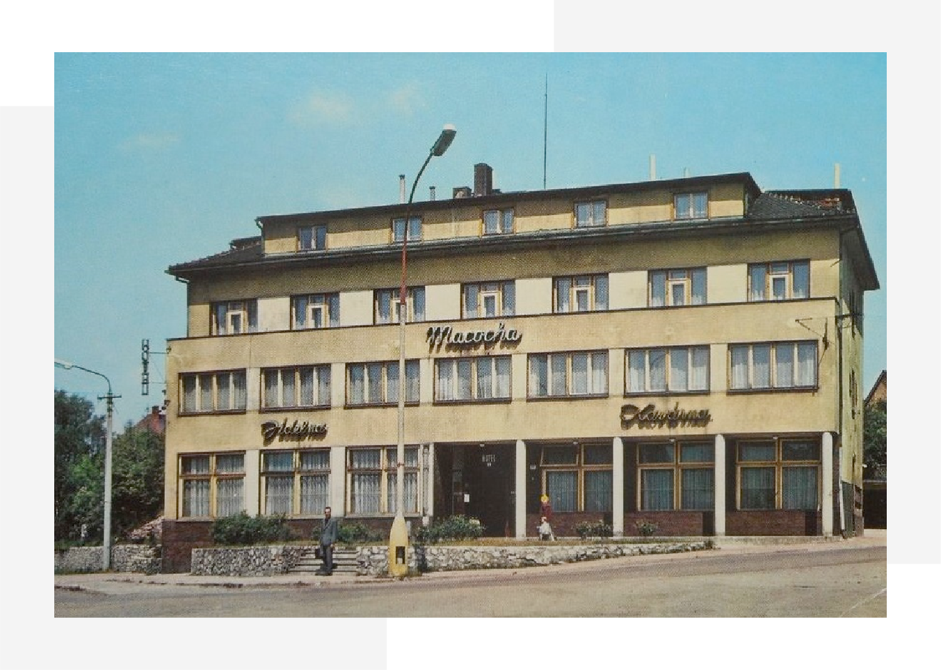 Retro three-story hotel building with multiple windows, signs, and two people near the entrance.